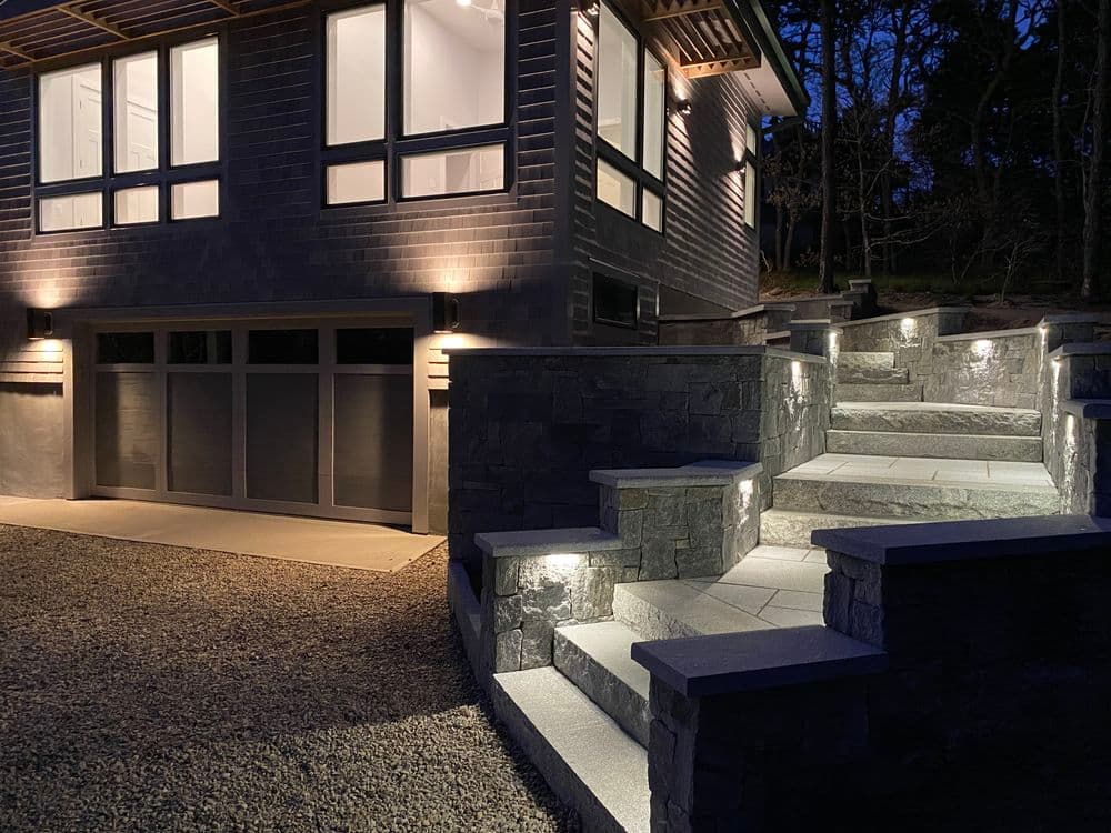Modern home exterior at night with lit stone steps and architectural lighting.
