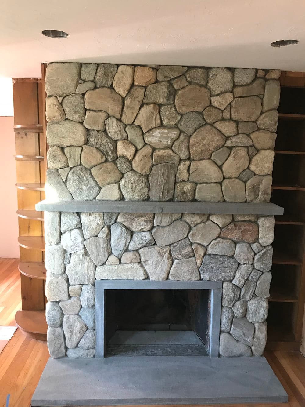 Stone fireplace with a rustic design, featuring a sturdy mantel and wooden shelves nearby.
