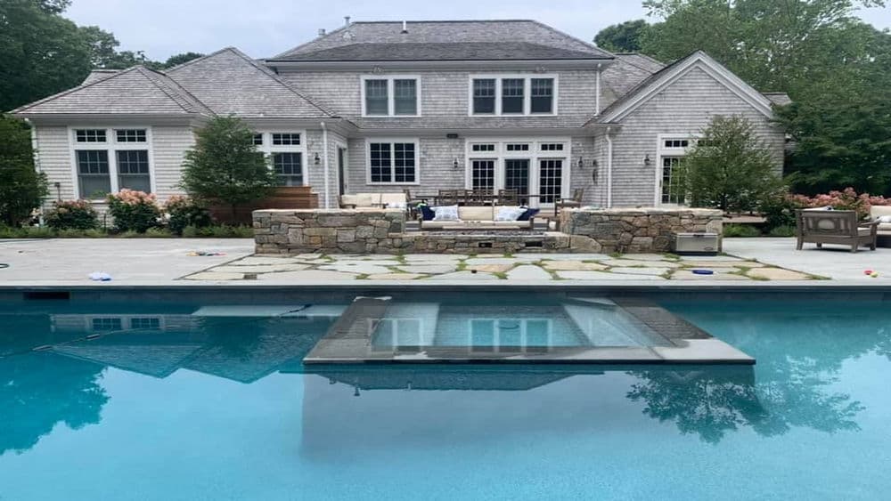 Luxury backyard with a modern pool, stone patio, and elegant house surrounded by greenery.