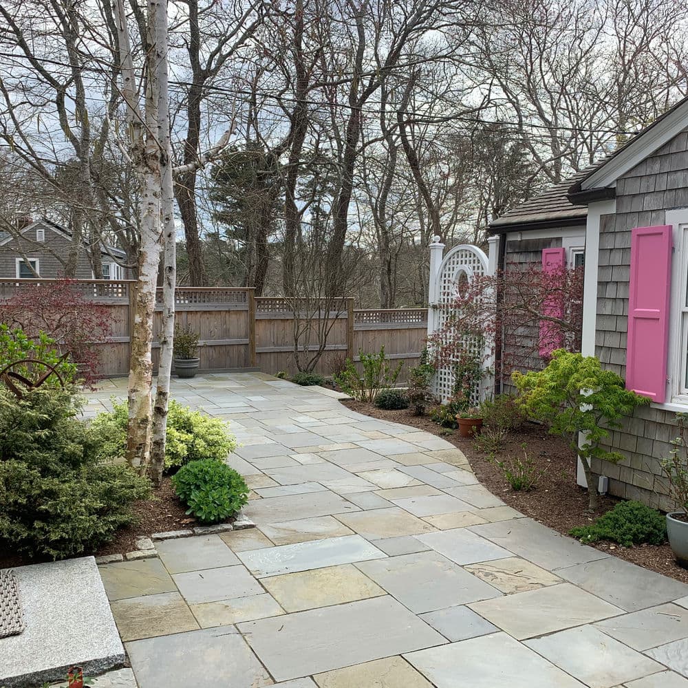 Beautiful stone patio with garden, birch trees, and pink shutters in a serene outdoor setting.