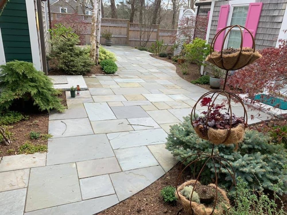 Stone patio pathways with landscaped garden and decorative plant stand in a residential backyard.