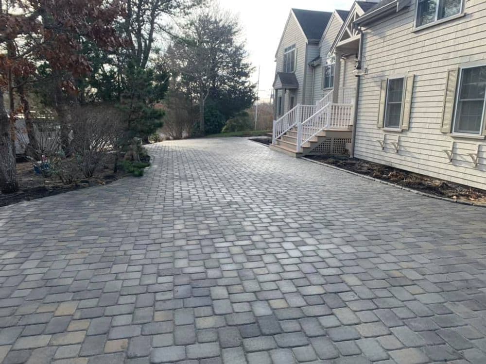Paved driveway with interlocking stones beside a house and landscaped garden.