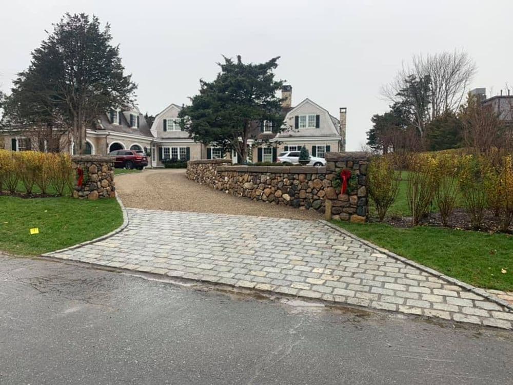 Elegant home with stone walls, festive greenery, and a picturesque driveway on a cloudy day.