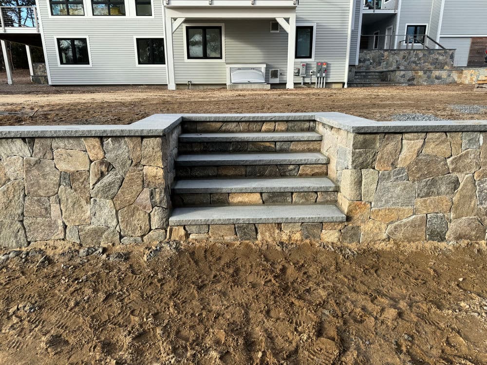 Stone steps leading to a modern home, featuring a decorative stone wall and a gravel pathway.