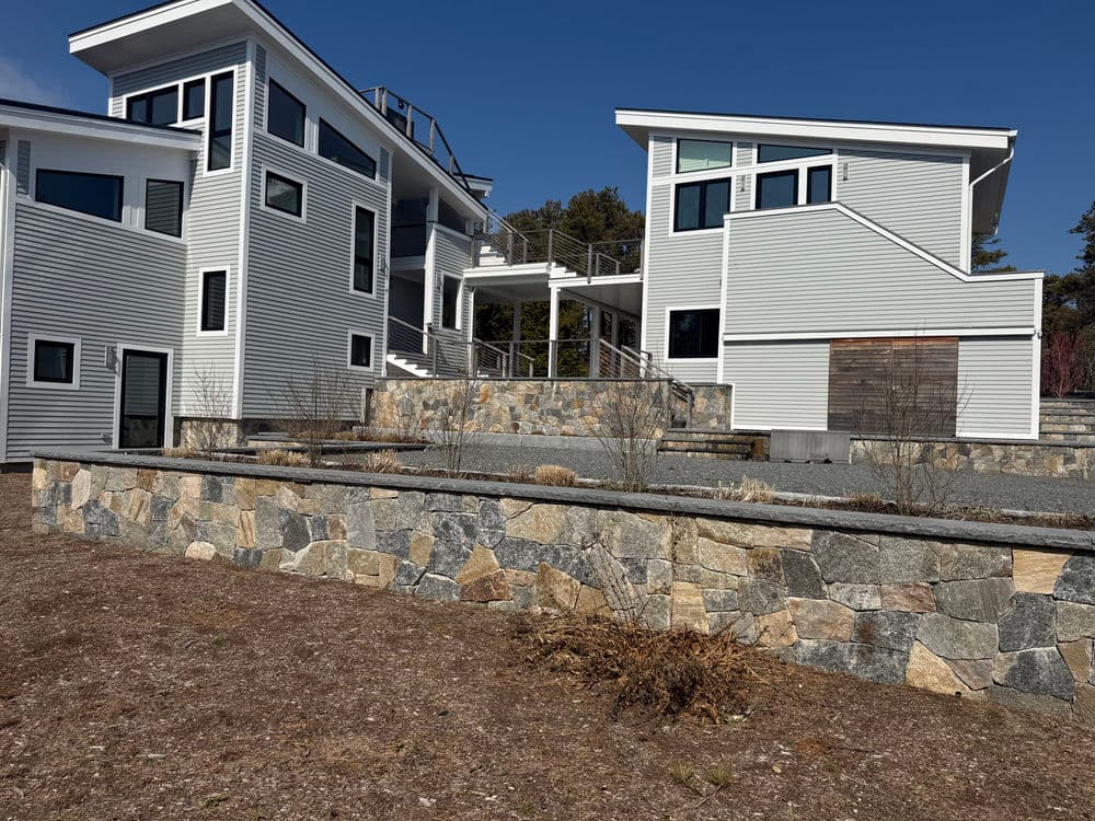 Modern two-story house with unique architecture and stone landscaping in a sunny setting.