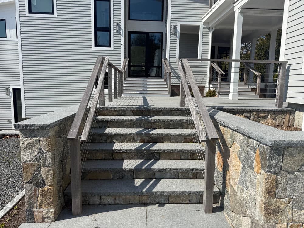 Modern house entrance with stone steps and wooden railings surrounded by landscaped area.
