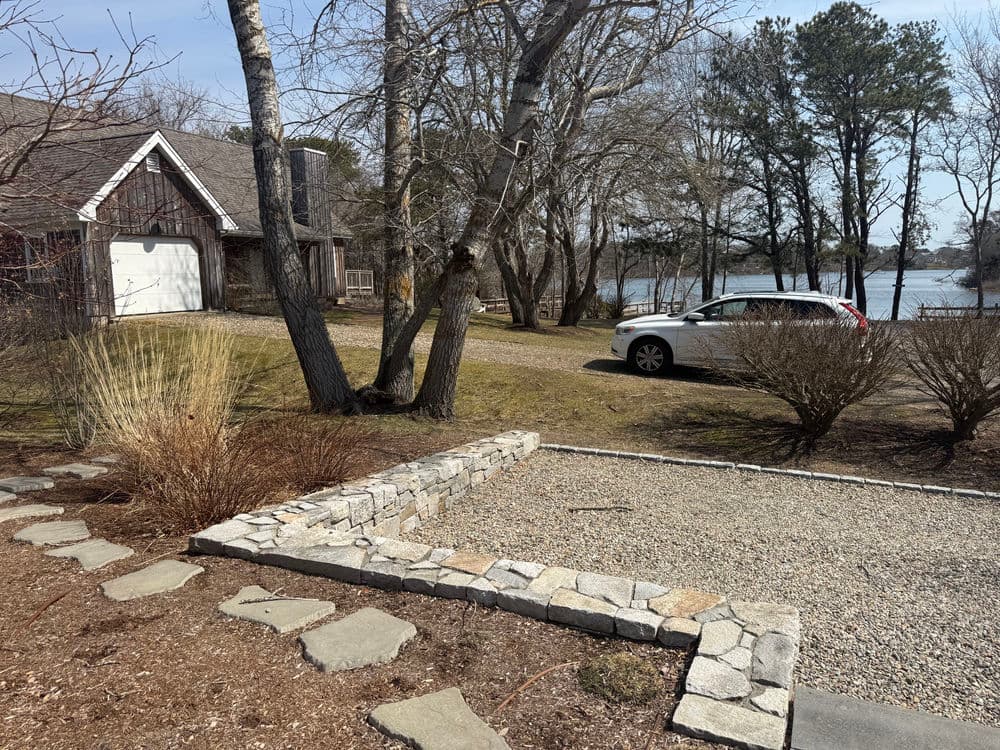 Scenic lakeside property with a car parked, trees, and landscaped garden features.